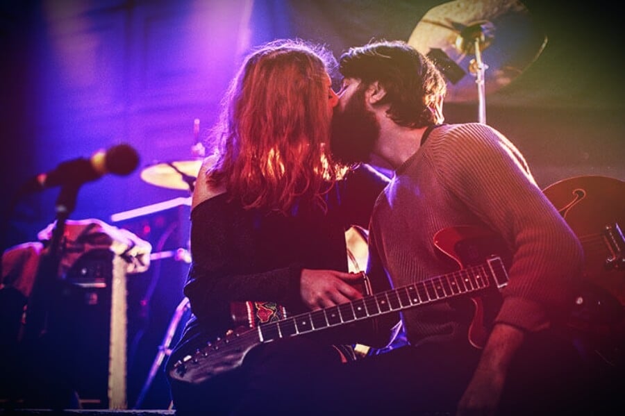 Next Tribe an older woman and her younger husband kiss on stage at a rock concert